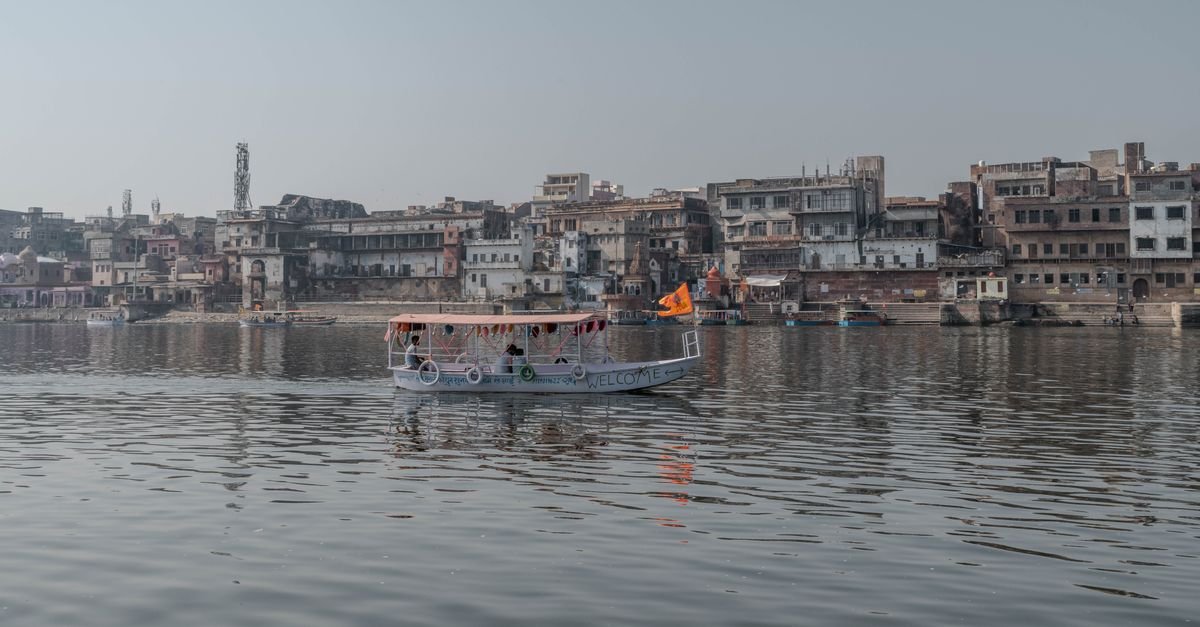 Boat cruising on the Yamuna River with Mathura cityscape in Uttar Pradesh, India.