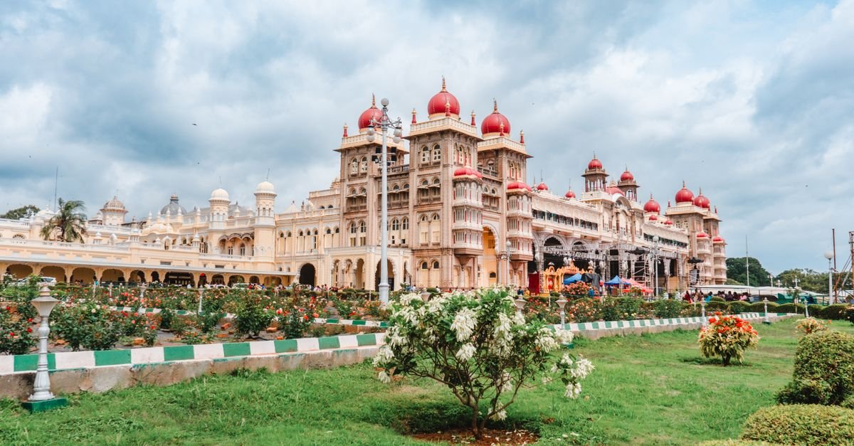 Stunning view of Mysore Palace in Karnataka, showcasing its ornate architecture and lush gardens under a cloudy sky.