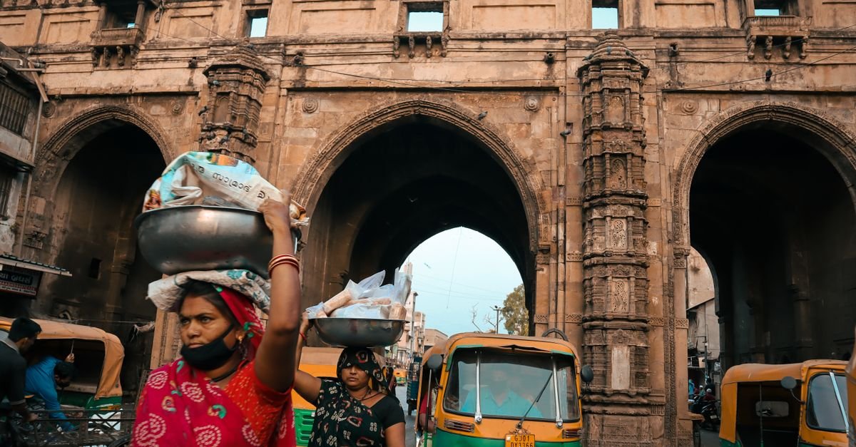 Street vendors and auto-rickshaws bustle by a historic gate in Ahmedabad, India.
